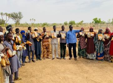 A mercy corps team member speaks to a large circle of nigerien farmers.