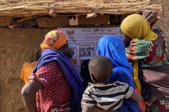A group of Nigerien women and children read a Mercy Corps poster.