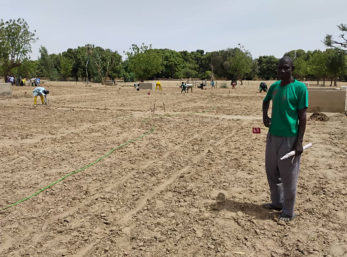 A nigerien farmer stands in a large field, in front of a number of workers.