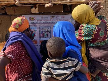 A group of Nigerien women and children read a Mercy Corps poster.